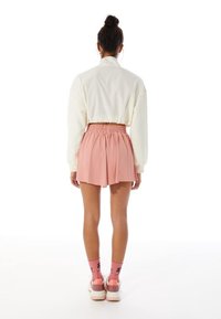 Sudadera blanca recortada, falda rosa con cintura elástica, calcetas rosas hasta la rodilla y zapatillas blancas gruesas; vista desde atrás.
