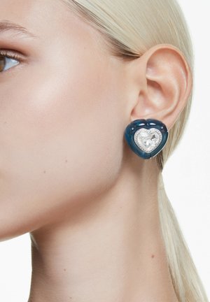 Tåreformede øreringe med en transparent blå resinbund og et hjerteformet klart krystalmidte, pyntet med små metalliske detaljer.