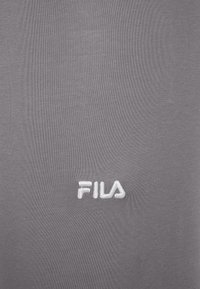 Szary materiał w tle z małym, białym, haftowanym logo FILA na środku.