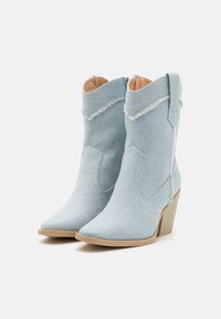 Světle modré denimové kotníkové boty s špičatou špičkou, roztrhaným vroubkovaným lemem a hnědým podpatkem. Hladká textura s bočními poutky.