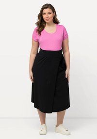 Roze top met korte mouwen met polka dots, gecombineerd met een zwarte wikkelrok met een zijstrik, en witte sneakers. Glad materiaal en een ontspannen pasvorm.