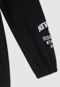 Czarne spodnie dresowe z elastycznymi mankietami, zdobione białym nadrukiem z napisem "NOWY JORK" oraz "WYSOKI ATLETA". Miękka tekstura materiału.