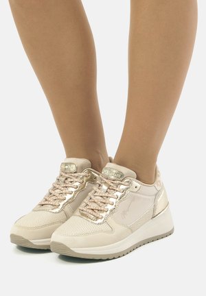 Baskets de sport beige avec des accents métalliques, maillage texturé et lacets plats. Semelle rembourrée et logo sur le côté.