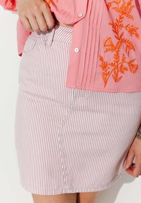 Blouse rose avec broderie florale orange, accompagnée d'une jupe en denim rayée rose clair et blanche. Gros plan sur la texture et la coupe de la jupe.