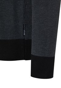 Schwarz-grauer Strickpullover mit strukturierter Musterung, gerippten Bündchen und einem kleinen Markenetikett an der Seite.