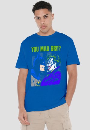 Young man wears blue shirt depicting Batman and Joker facing each other with text "YOU MAD BRO?" above them.