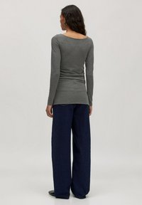 Grijze longsleeve top met een ruime halslijn, getailleerd in de taille, gecombineerd met losse donkerblauwe wijde pijpen jeans. Soepele textuur en casual ontwerp.