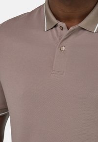 Polo tričko v taupe barvě s texturovaným povrchem, které má límeček, dva knoflíky a bílé kontrastní pruhy na límci.