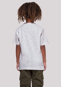 Camiseta de algodón gris de manga corta, corte relajado y cuello redondo, combinada con pantalones cargo verdes oliva, vista desde atrás.