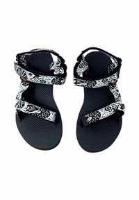 Chanclas negras con correas blancas estampadas. Plantilla texturizada y hebillas ajustables. Diseño ligero y abierto ideal para el verano.