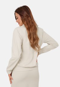 Jasnobeżowy sweatshirt o luźnym kroju, z prążkowanymi mankietami i elastycznym pasem. Gładki materiał o prostym, nieskomplikowanym wzornictwie.