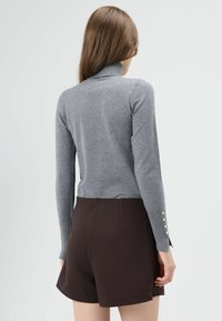 Grijze coltrui met lange mouwen, een aansluitend model en gouden knopen aan de manchetten, gecombineerd met een bruine korte broek.