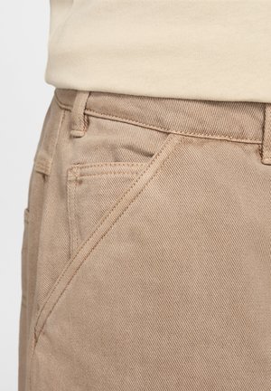 Beige Baumwollhosen mit glatter Textur, schrägen Fronttaschen und sichtbaren Nähten entlang der Nähte.