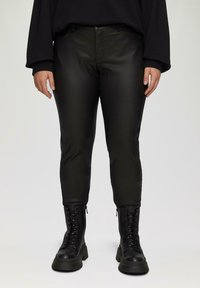Zwarte nep leren broek met een slim fit, voorzien van zakken en een gladde textuur. Gecombineerd met zwarte veterschoenen en een losse zwarte top.