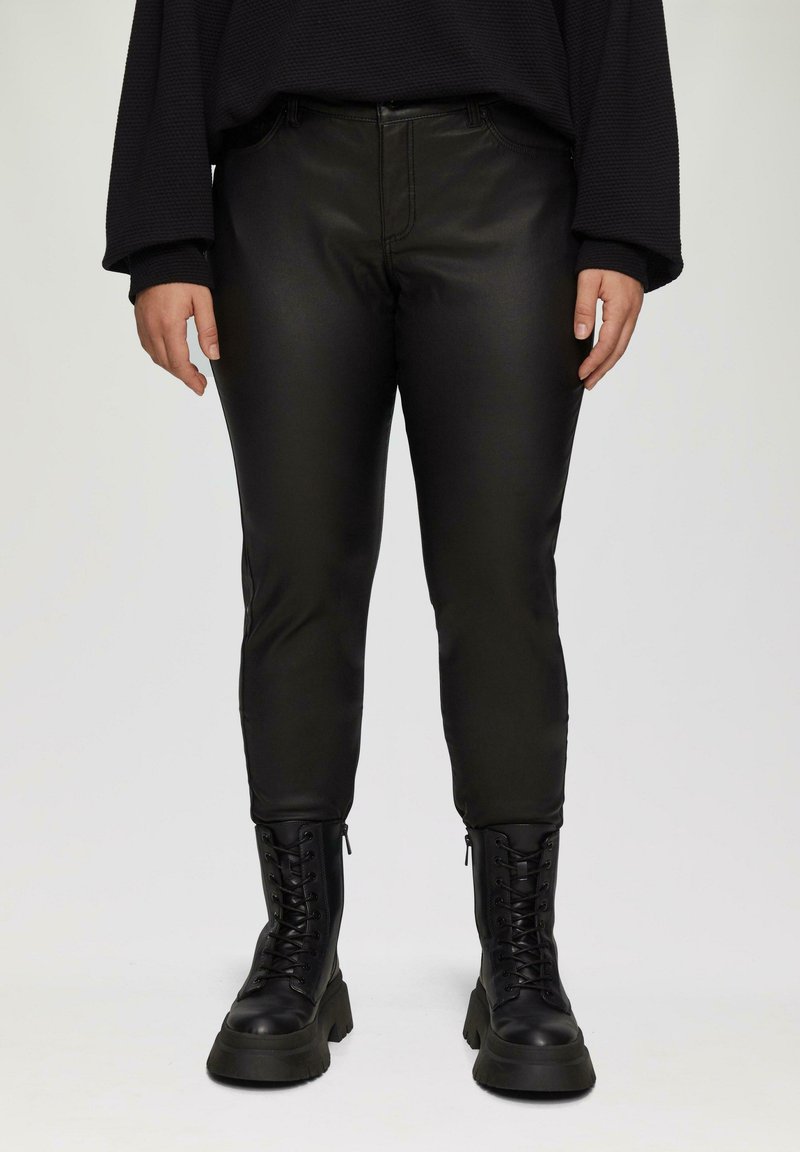Zwarte nep leren broek met een slim fit, voorzien van zakken en een gladde textuur. Gecombineerd met zwarte veterschoenen en een losse zwarte top.