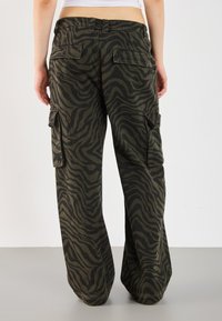 Cargo pants featuring a green and black zebra stripe pattern, with wide legs, pockets on the sides, and a relaxed fit.