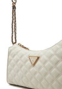 Borsa a tracolla trapuntata color crema con catena dorata. Presenta una placca con logo triangolare, chiusura a zip e dettagli sulla superficie texturizzati.