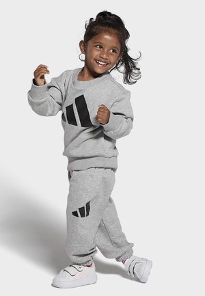 Conjunto de sudadera y pantalones de chándal grises con acentos de logo negros. Material acogedor, corte relajado, puños y dobladillo acanalados. Zapatillas blancas con acentos rosas.