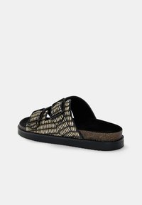 Svart och beige slidesandal med två justerbara remmar, en texturerad ovandel och en korkliknande mellansula med en kontrasterande svart yttersula.