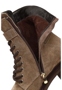 Bottes à cheville en suède marron avec une fermeture éclair sur le côté, doublure en marron texturé et garniture en cuir foncé le long du bord. Possède des œillets en métal et des lacets.