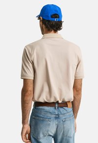 Beige polo-shirt med korte ærmer, kombinert med lyseblå jeans og en blå caps. Brun belte synlig i livet, med et teksturert mønster.