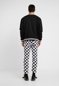 Svart bomberjacka med vita randiga manschetter och nederkant, ihop med svartvitt rutig byxor. Svarta sneakers fulländar outfiten.