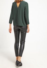 Grøn satinbluse med dyb V-ryg, parret med shiny sorte faux læder leggings og lavhælede sorte sko. Elegant, tætsiddende silhuet.