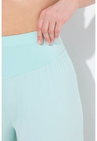 Lichtblauwe, rekbare sportbroek met een brede, ribbelige tailleband. Close-upweergave die de gladde textuur en subtiele plooien benadrukt.