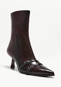 Ankle boot z wąskim noskiem w błyszczącej burgundowej skórze. Posiada dwa regulowane paski z srebrnymi klamrami oraz smukły obcas. Gładka tekstura, minimalistyczny design.