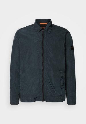 Schwarze, leichte Jacke mit Reißverschluss, spitzem Kragen und zwei Seitentaschen. Strukturierter Stoff und elastische Bündchen. Branding am Ärmel.