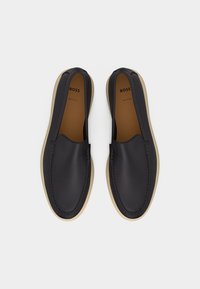 Paire de chaussures en cuir noir à enfiler avec semelles beiges, bouts arrondis et logo de marque « BOSS » à l’intérieur de chaque chaussure.