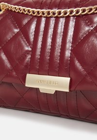 Bordeauxfarvet quiltet lædertaske med en guldkæde som rem og en metalplade med mærke. Har en struktureret, polstret overflade og et struktureret design.