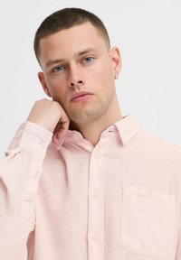 Chemise boutonnière rose clair en tissu texturé avec une petite poche poitrine et un col. Offre une coupe décontractée et des manches retroussables.