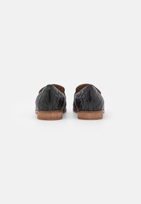 Černé prošívané loafers s hladkým povrchem, s přírodně dřevěným podpatkem a otevřenými stranami, zdůrazňující klasický a elegantní design.