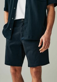 Marineblaue Baumwollbluse und passender Shorts. Die Bluse hat kurze Ärmel und Knöpfe, während die Shorts einen klassischen Schnitt und seitliche Taschen haben.