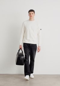 Witte katoenen sweatshirt met ronde hals, zwarte jeans en witte sneakers. Draagt een zwarte leren tas met een rits.