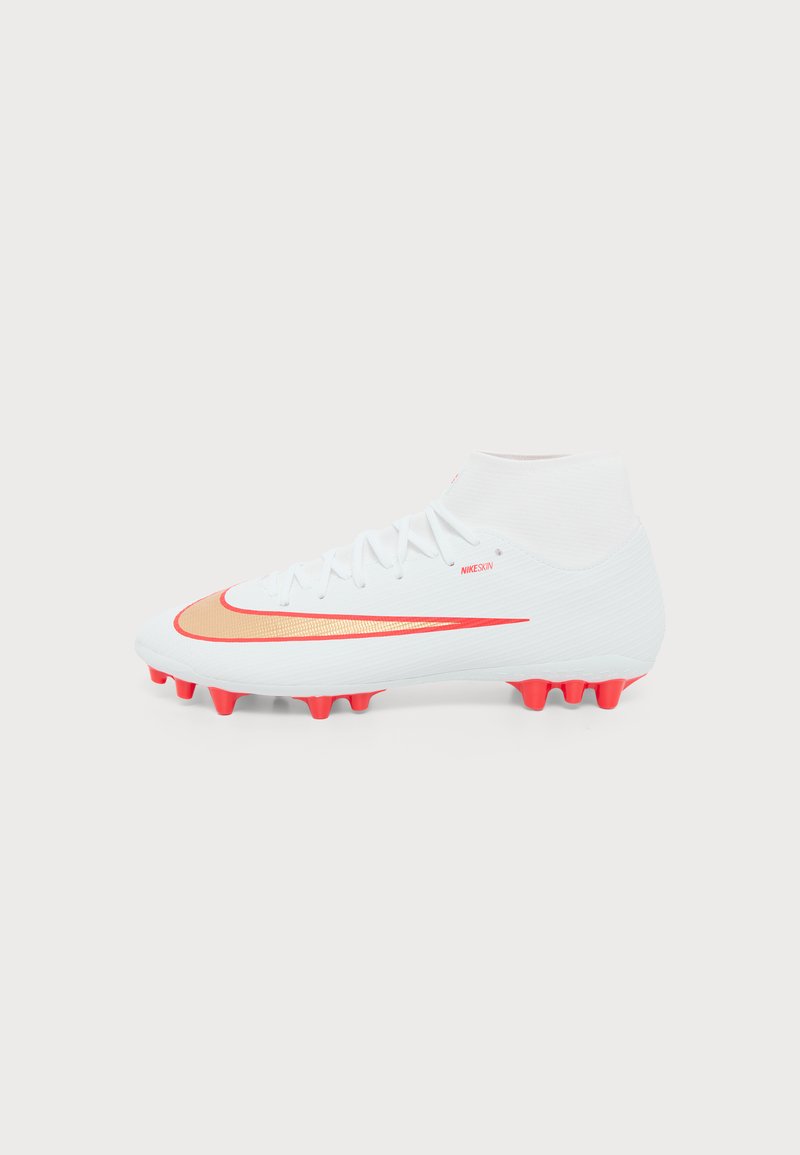 Λευκό ποδοσφαιρικό παπούτσι Nike με κόκκινες τάπες, κόκκινο λογότυπο swoosh και μεσαίο κολάρο σε απλό ανοιχτό φόντο.