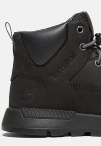 Bottine Timberland noire à la cheville avec col matelassé, œillets métalliques hexagonaux, logo embossé et semelle épaisse en caoutchouc pour une utilisation en extérieur.