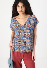 Short-sleeve V-neck top in a multicolored floral and abstract pattern featuring blue, red, and black accents on lightweight fabric.
