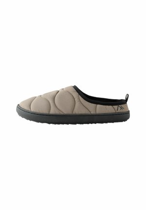 Quilted beige slipper with a rounded toe, black trim, and textured rubber sole. Features subtle stitching and a pull tab at the back.