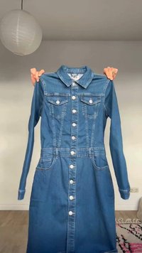 Käed hoidmas sinist teksariidest pika varrukaga kleiti, millel on ees nupud, rinnataskud ja küljetaskud, taustaks tavalise seina taust.