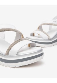 Sandalias de plataforma blancas con tiras metálicas entrelazadas, acentos plateados y una suela texturizada en blanco y gris. Material superior suave.