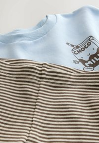 Svijetlo plava dukserica s grafikom Choco Milk, u kombinaciji s horizontalno prugastim smeškim i kremastim materijalom ispod. Mekana tekstura, ležeran dizajn.