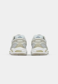 Vita och grå atletiska skor med övre del i mesh, Gel-dämpning, vadderad krage och texturerad yttersula för grepp, med en beige accent.