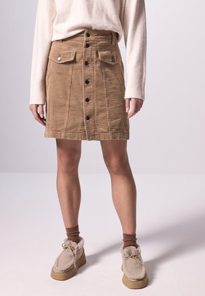 Bruine corduroy rok met knoopsluiting aan de voorkant, zijzakken en gestructureerde stof. Gepaarde met beige fluffy schoenen en bruine sokken.