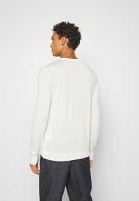 White long-sleeve sweater with a round neckline, soft texture, and ribbed cuffs, paired with dark, loose-fitting denim trousers.