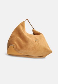 Sac en daim beige à la forme souple, doté d'une base en cuir lisse, d'une poignée unique et d'un accent métallique à l'avant.