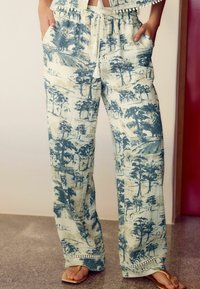 Pantaloni larghi e a fantasia in tessuto leggero, con disegni paesaggistici blu. Vita con cordoncino, tasche e pizzo lungo l'orlo.