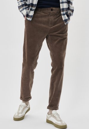 Brown corduroy pants with a straight cut and slight tapering, featuring a button closure and rolled cuffs, paired with white sneakers.