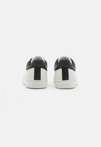 Sneaker bianco e nero con tomaia in pelle liscia, forma arrotondata e striscia nera centrale. "GUESS" impresso sul tallone.